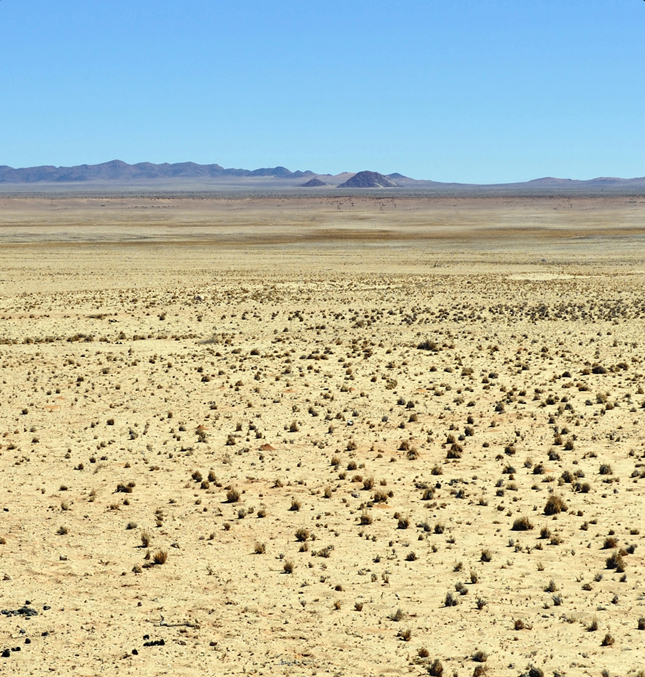 Vast desert with barren mountains in the background under a blue sky.